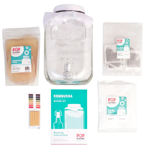 Kombucha brewing kit with glass jar, SCOBY, tea, sugar, pH strips, and packaging on a white background